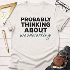 Women's funny woodworking graphic tee shirt for female woodworkers, makers, and DIY builders — Sawdust & Ponytails. White cotton tee with "PROBABLY THINKING ABOUT woodworking" text.