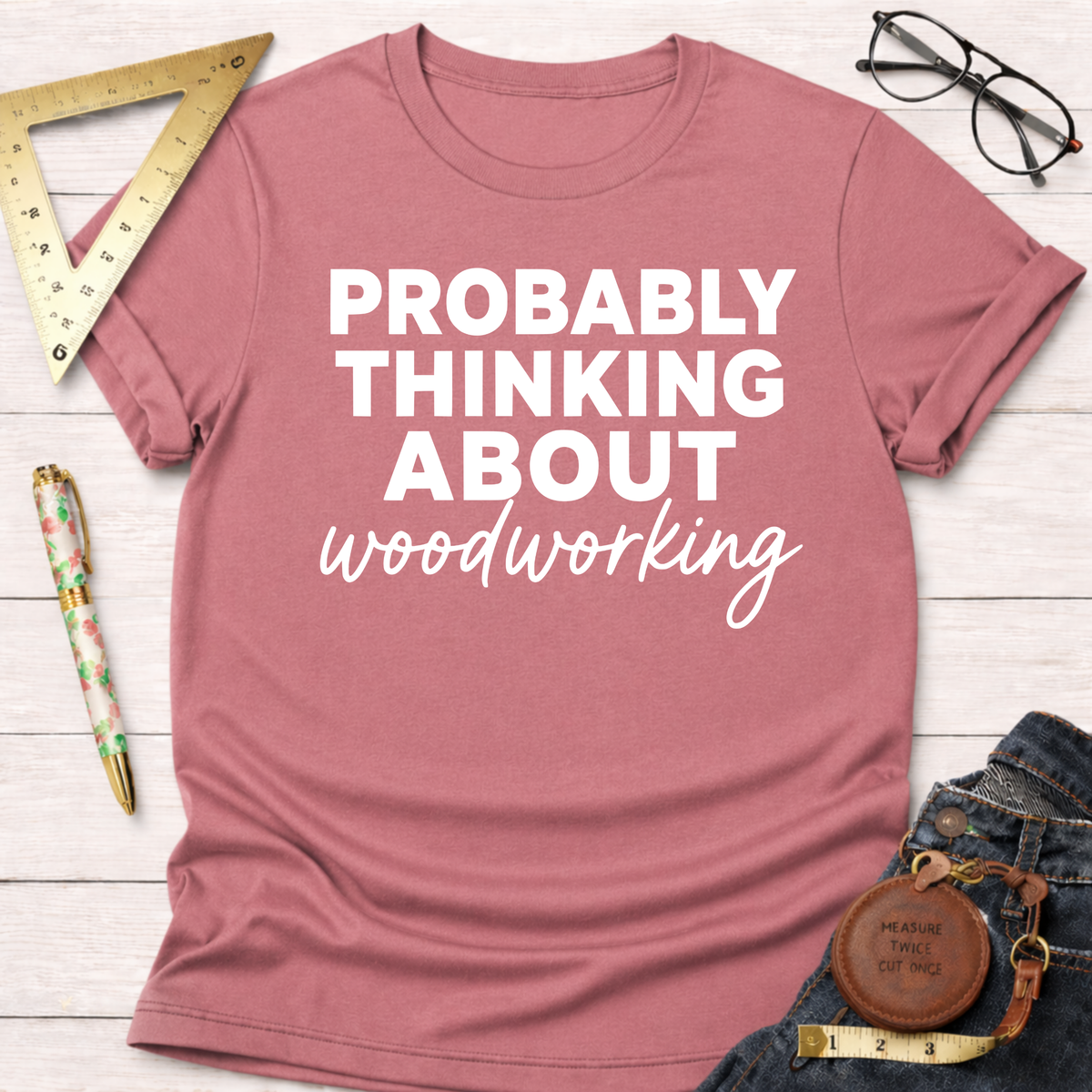 Women's funny woodworking graphic tee shirt for female woodworkers, makers, and DIY builders — Sawdust & Ponytails. Mauve pink short-sleeve tee with "PROBABLY THINKING ABOUT woodworking" in white text.