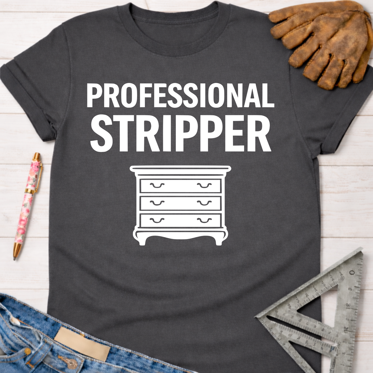 Women's funny woodworking graphic tee shirt for female woodworkers, makers, and DIY builders — Sawdust & Ponytails. Dark gray cotton tee with "PROFESSIONAL STRIPPER" text and a dresser icon.