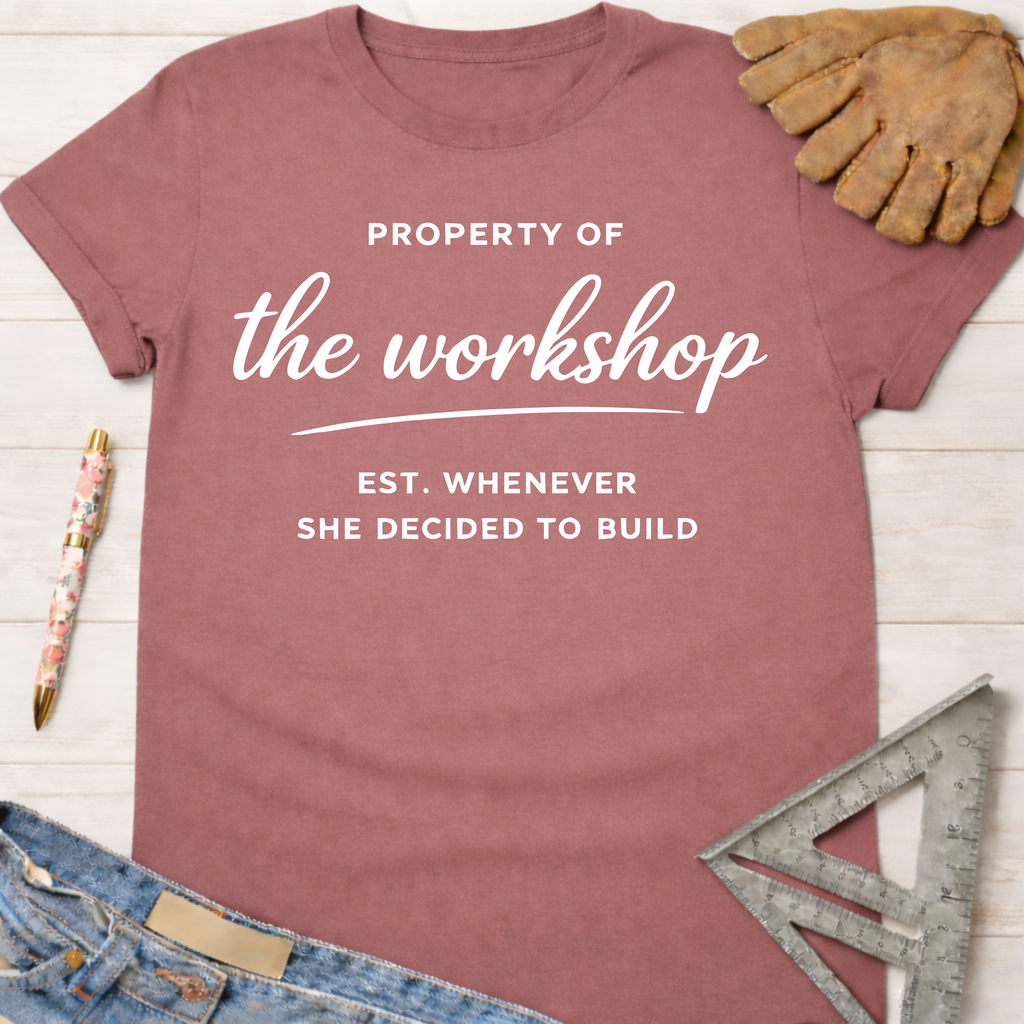 Women's funny woodworking graphic tee shirt for female woodworkers, makers, and DIY builders — Sawdust & Ponytails. Mauve t-shirt with "Property of the workshop EST. WHENEVER SHE DECIDED TO BUILD" in white text.