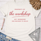 Women's funny woodworking graphic tee shirt for female woodworkers, makers, and DIY builders — Sawdust & Ponytails. Cream t-shirt with "Property of the workshop EST. Whenever She Decided to Build" in red script.