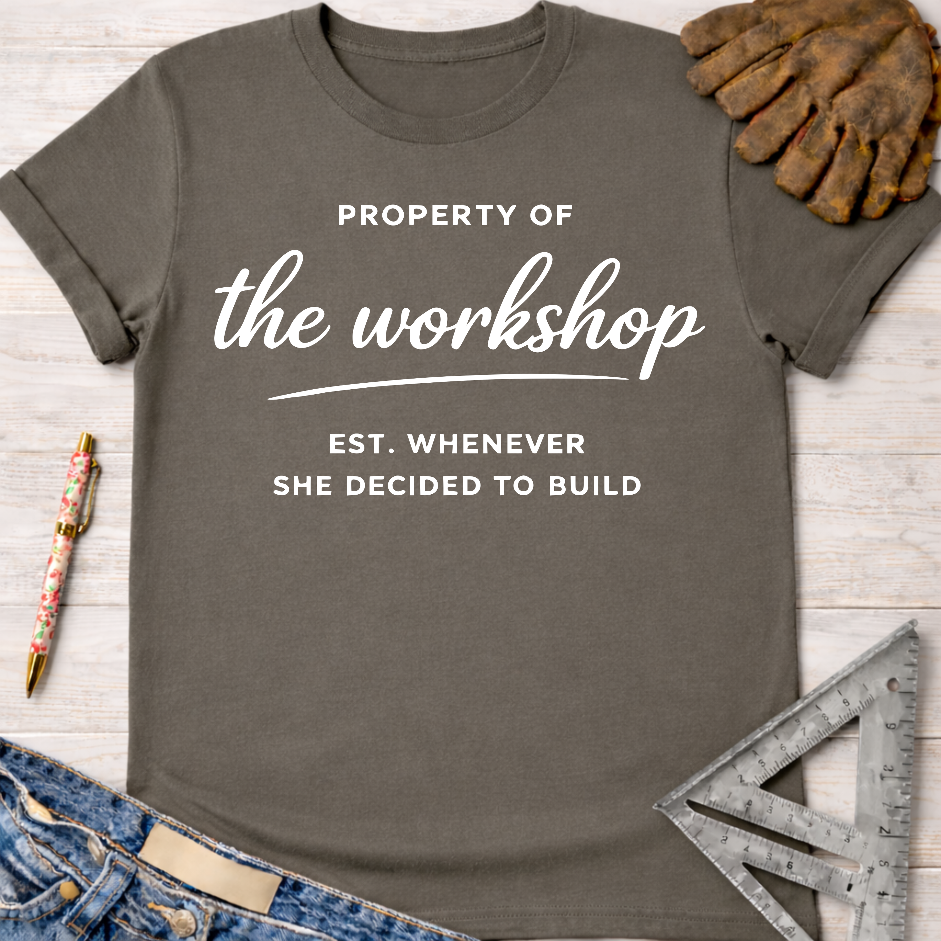 Women's funny woodworking graphic tee shirt for female woodworkers, makers, and DIY builders — Sawdust & Ponytails. Dark gray t-shirt with "Property of the workshop EST. WHENEVER SHE DECIDED TO BUILD" in white text.