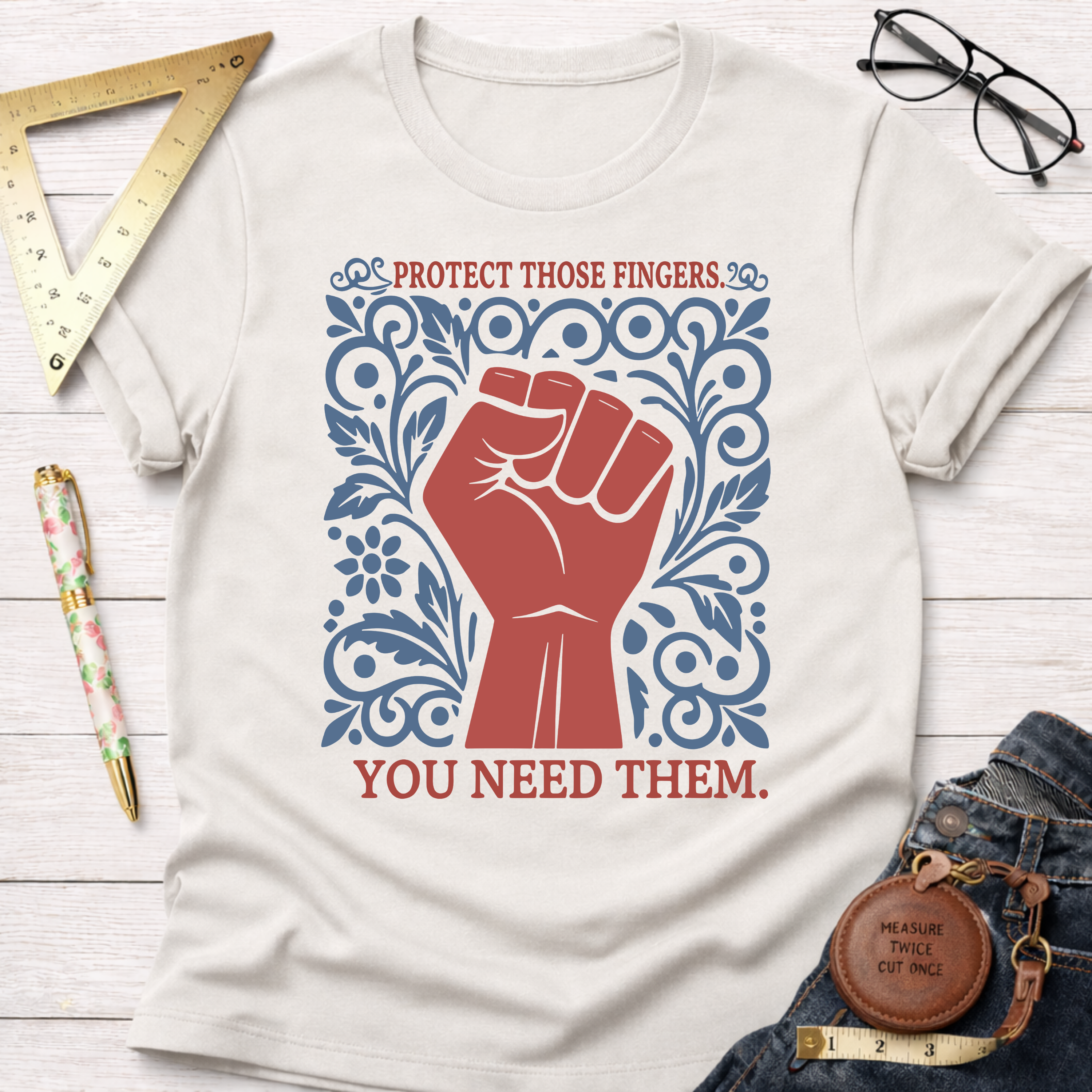 Cream cotton t-shirt with a red fist and blue floral design, "Protect Those Fingers. You Need Them." text.
