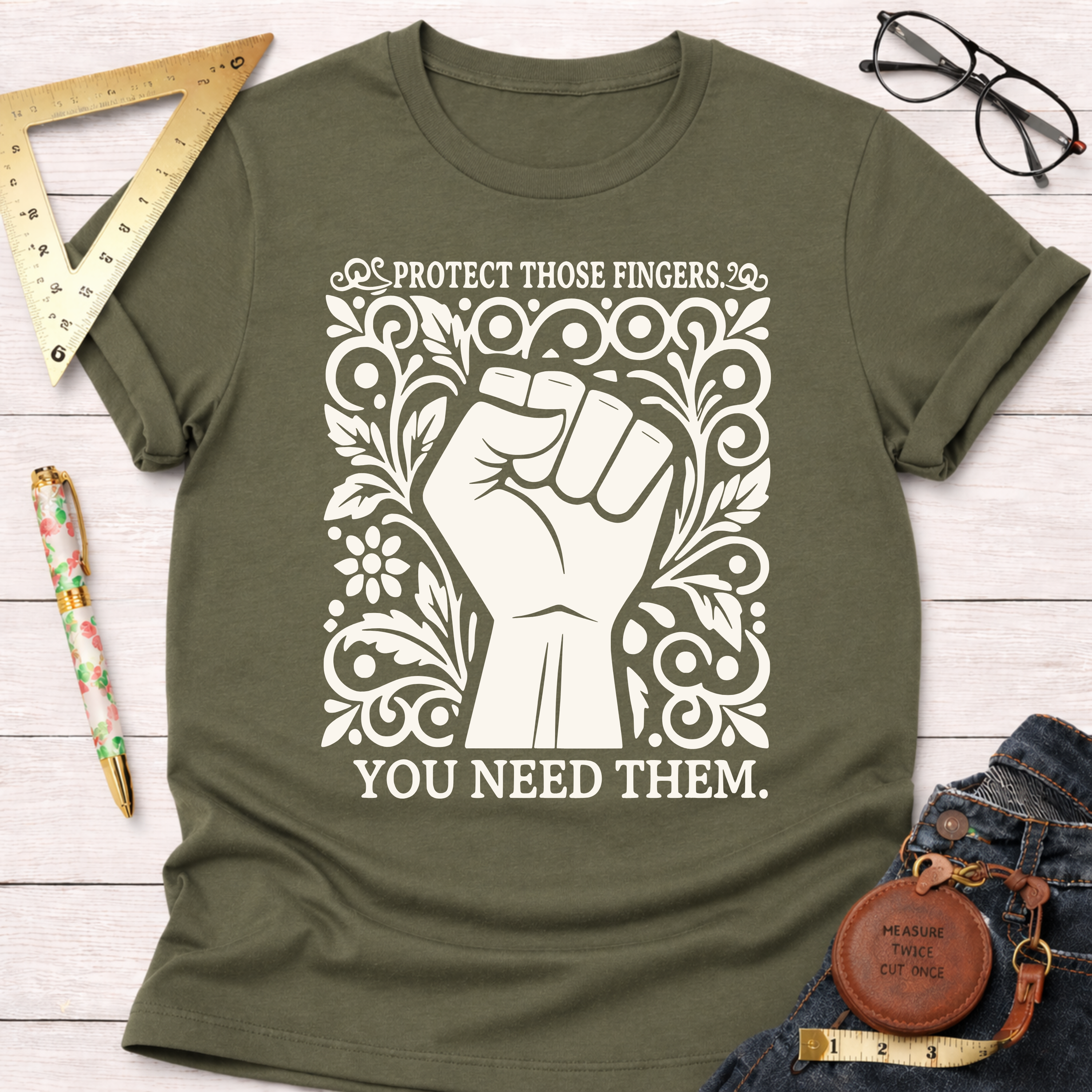 Olive green cotton t-shirt with a white graphic of a fist surrounded by ornate floral designs and the text "PROTECT THOSE FINGERS. YOU NEED THEM.