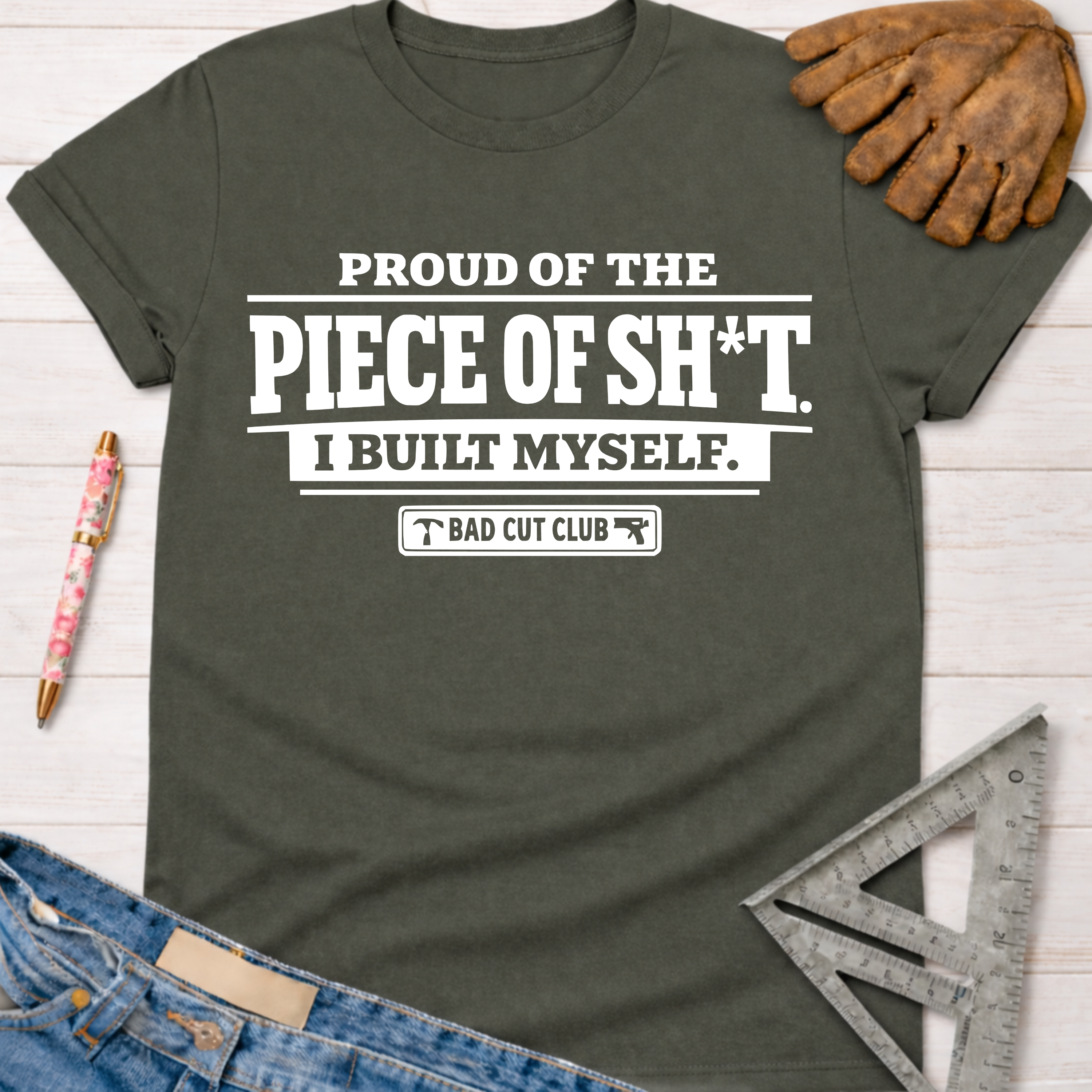 Women's funny woodworking graphic tee shirt for female woodworkers, makers, and DIY builders — Sawdust & Ponytails. Dark gray cotton tee with "Proud Of The Piece Of Sh*t I Built Myself. Bad Cut Club" in white text.