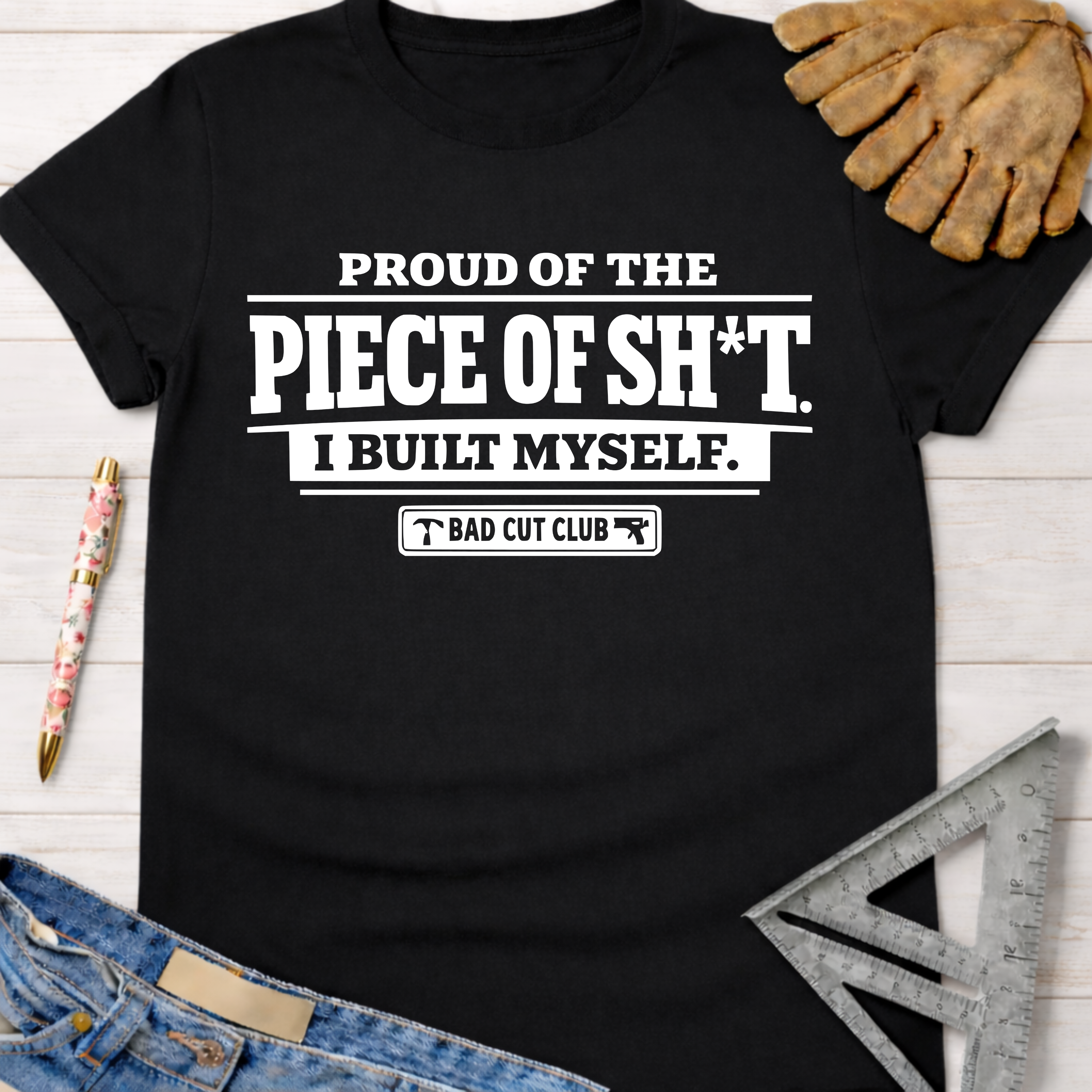 Black cotton women's funny woodworking graphic tee with "Proud Of The Piece Of Sh*t I Built Myself. Bad Cut Club" text. Sawdust & Ponytails.