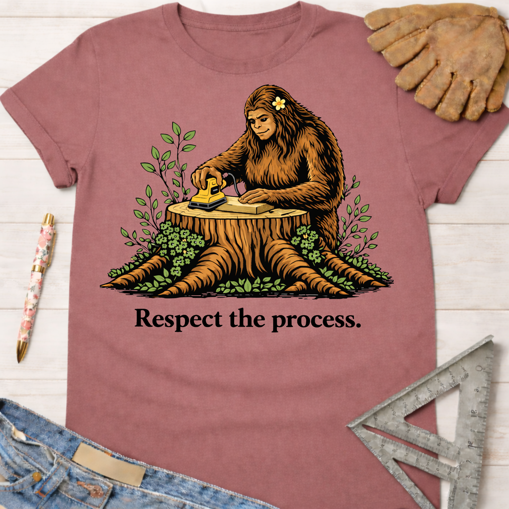 Women's funny woodworking graphic tee shirt for female woodworkers, makers, and DIY builders — Sawdust & Ponytails. Mauve cotton tee with Bigfoot sanding wood on a tree stump, "Respect the process." text.