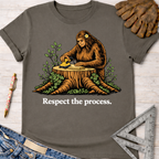 Women's funny woodworking graphic tee shirt for female woodworkers, makers, and DIY builders — Sawdust & Ponytails. Charcoal gray cotton tee with a Bigfoot sanding wood on a tree stump, "Respect the process." text.