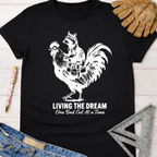 Women's funny woodworking graphic tee shirt for female woodworkers, makers, and DIY builders — Sawdust & Ponytails. Black cotton tee with a white graphic of a raccoon riding a rooster carrying tools, text "Living The Dream One Bad Cut At A Time".