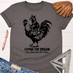 Charcoal gray unisex tee with a raccoon riding a rooster graphic, "Living The Dream One Bad Cut At A Time" text. Women's funny woodworking graphic tee shirt for female woodworkers, makers, and DIY builders — Sawdust & Ponytails