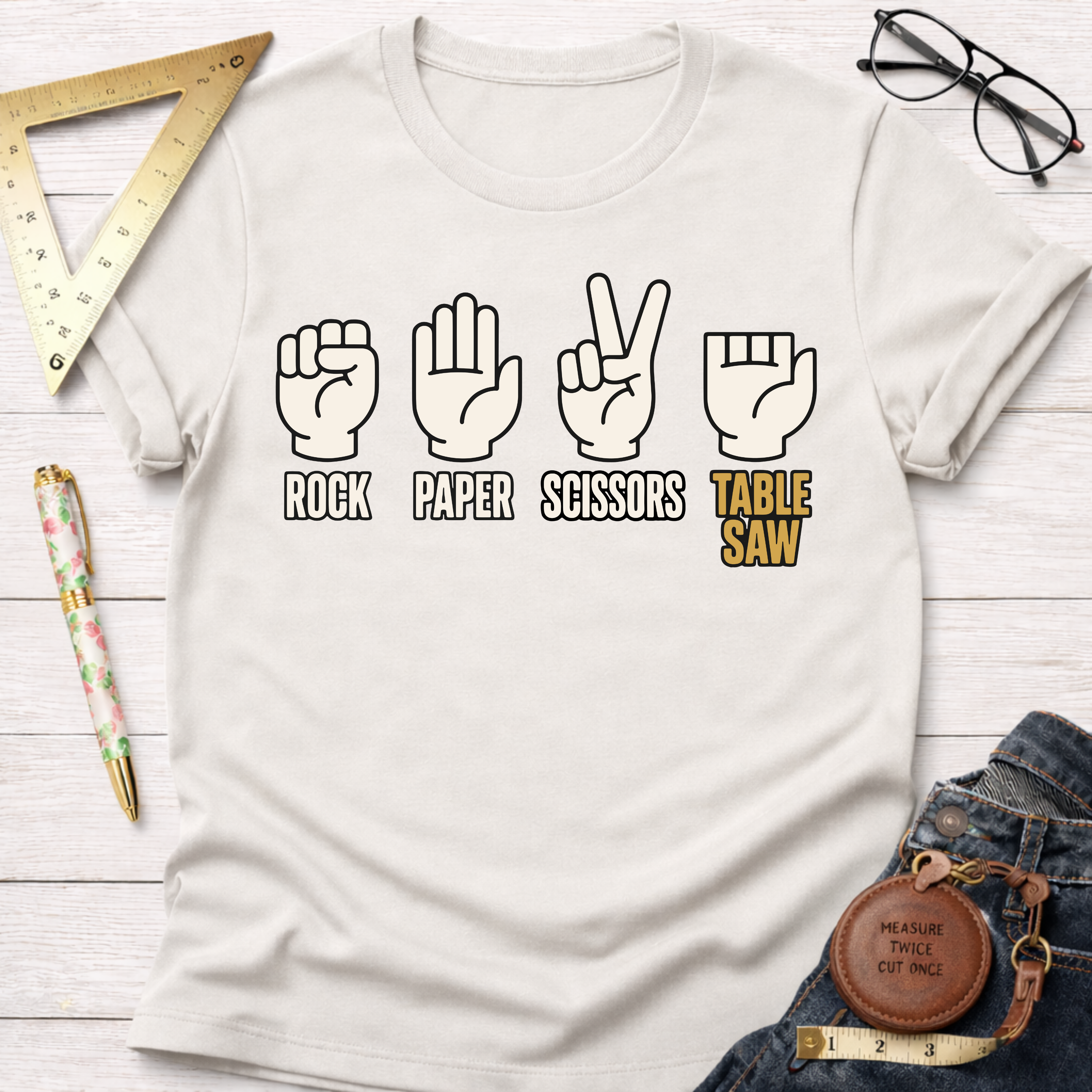 Cream t-shirt with "Rock Paper Scissors Table Saw" graphic featuring hand gestures and a table saw.