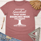 Women's funny woodworking graphic tee shirt for female woodworkers, makers, and DIY builders — Sawdust & Ponytails. Mauve cotton t-shirt with "Roots Down Sawdust In My Veins Branches Wide She Grows What She Builds" graphic.