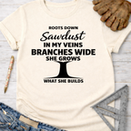 Women's funny woodworking graphic tee shirt for female woodworkers, makers, and DIY builders — Sawdust & Ponytails. Cream t-shirt with "Roots Down Sawdust In My Veins Branches Wide She Grows What She Builds" text and tree graphic.