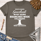 Women's funny woodworking graphic tee shirt for female woodworkers, makers, and DIY builders — Sawdust & Ponytails. Dark gray cotton tee with "Roots Down Sawdust In My Veins Branches Wide She Grows What She Builds" text and a tree graphic.