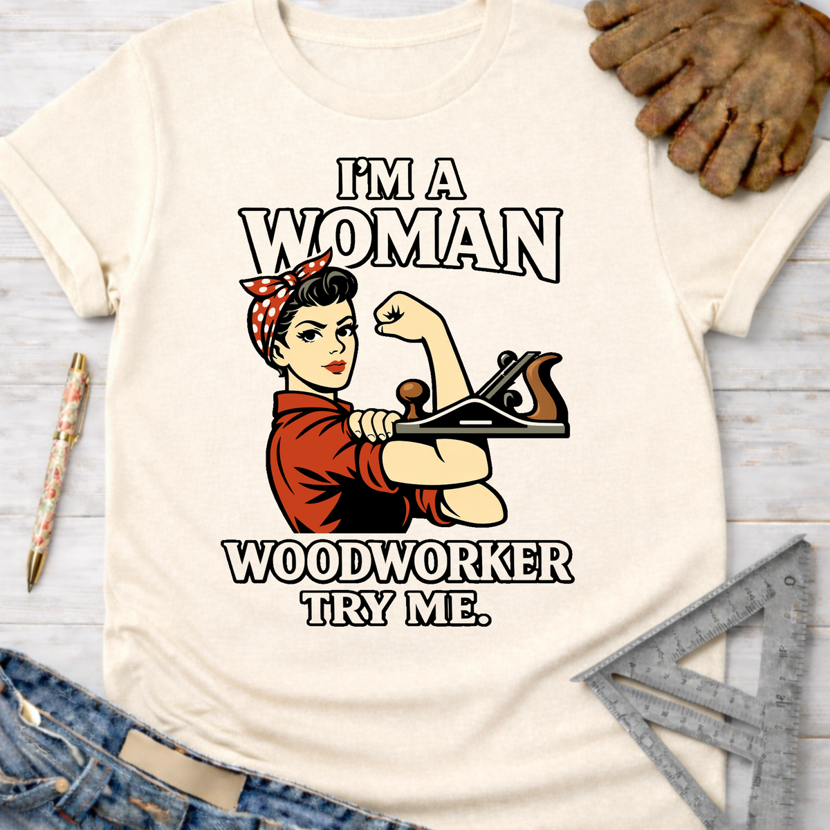 Women's funny woodworking graphic tee shirt for female woodworkers, makers, and DIY builders — Sawdust & Ponytails. Cream t-shirt with Rosie the Riveter holding a wood plane and "I'm A Woman Woodworker Try Me" text.