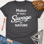 Women's funny woodworking graphic tee shirt for female woodworkers, makers, and DIY builders — Sawdust & Ponytails. Dark gray cotton tee with "Maker by Skill Savage by Nature" in white text.
