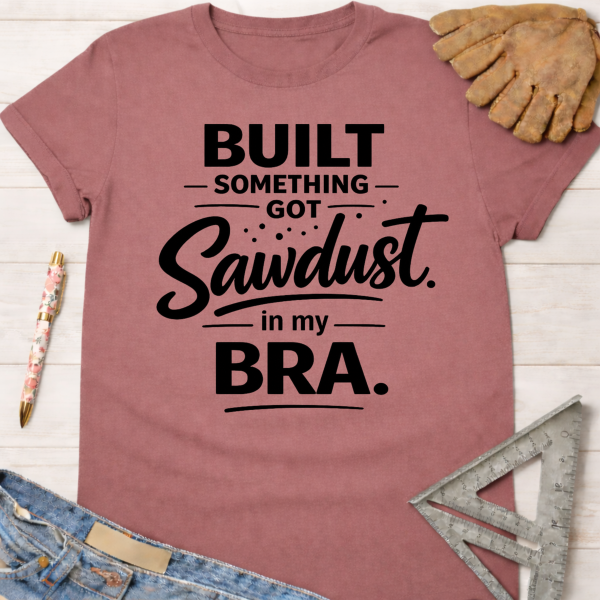 Women's funny woodworking graphic tee shirt for female woodworkers, makers, and DIY builders — Sawdust & Ponytails. Mauve cotton t-shirt with "Built Something Got Sawdust in my Bra" text.