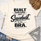 Women's funny woodworking graphic tee shirt for female woodworkers, makers, and DIY builders — Sawdust & Ponytails. Cream short-sleeve t-shirt with "Built Something Got Sawdust in my Bra" in black text.