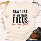 Cream cotton t-shirt with "SAWDUST IN MY HAIR FOCUS in my soul" text, styled with jeans and tools.