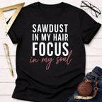 Black cotton t-shirt with "SAWDUST IN MY HAIR FOCUS in my soul" text, styled with jeans and tools.