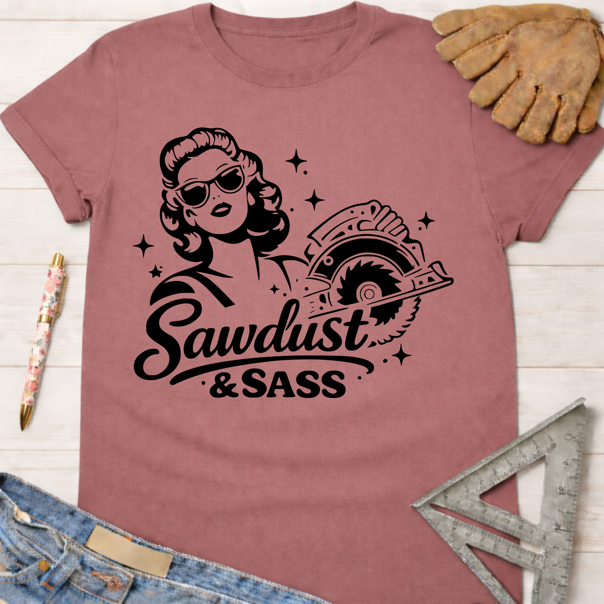 Women's funny woodworking graphic tee shirt for female woodworkers, makers, and DIY builders — Sawdust & Ponytails. Mauve cotton tee with a retro woman holding a circular saw and "Sawdust & Sass" text.