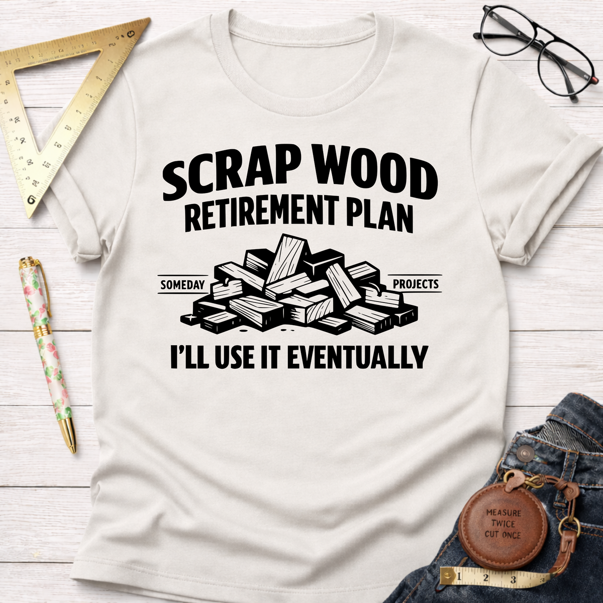 Off-white t-shirt with "Scrap Wood Retirement Plan" text, wood pile graphic, and "I'll Use It Eventually.