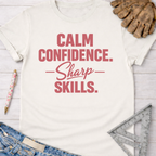 Women's funny woodworking graphic tee shirt for female woodworkers, makers, and DIY builders — Sawdust & Ponytails. Cream cotton tee with "Calm Confidence. Sharp Skills." in red.
