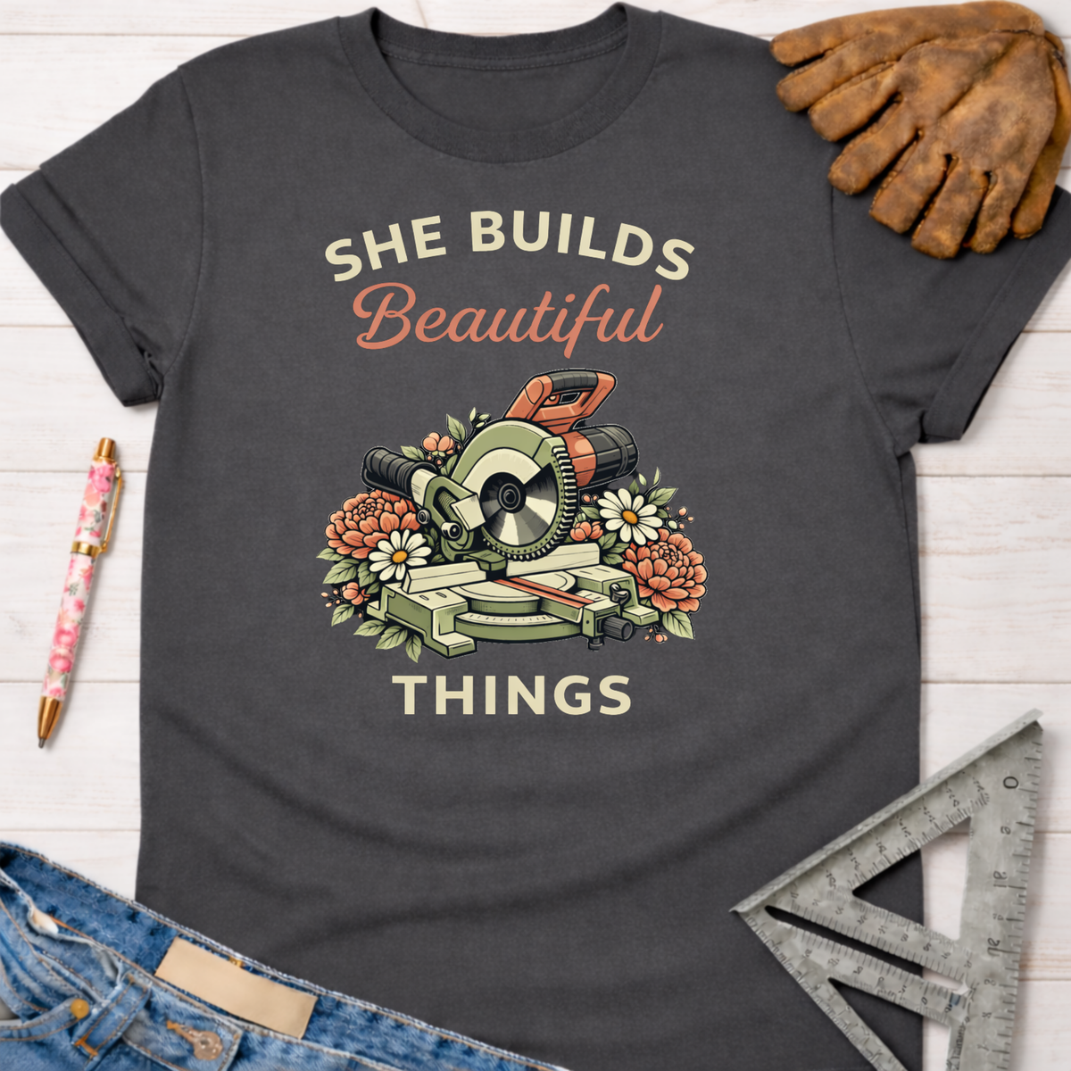 Charcoal gray cotton tee with "She Builds Beautiful Things" and miter saw floral graphic. Women's funny woodworking graphic tee shirt for female woodworkers, makers, and DIY builders — Sawdust & Ponytails.