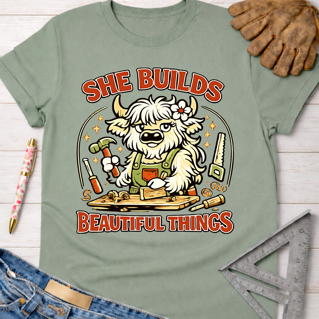 Women's funny woodworking graphic tee shirt for female woodworkers, makers, and DIY builders — Sawdust & Ponytails. Light green cotton tee with a cartoon highland cow building wood.