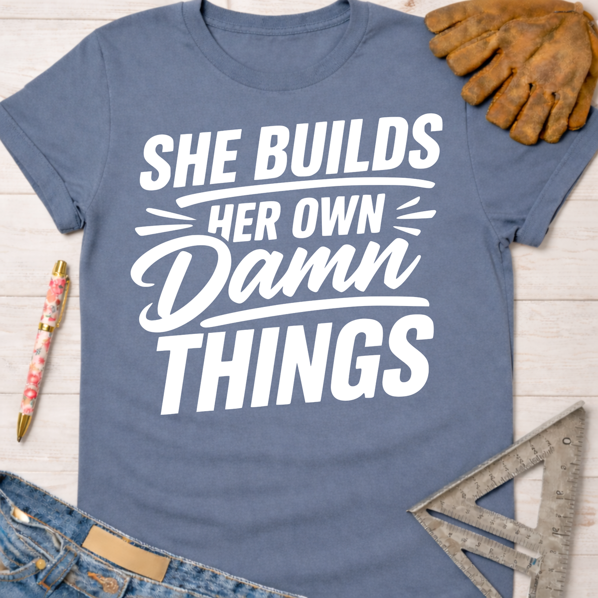 Blue cotton tee with "She Builds Her Own Damn Things" graphic. Women's funny woodworking graphic tee shirt for female woodworkers, makers, and DIY builders — Sawdust & Ponytails.