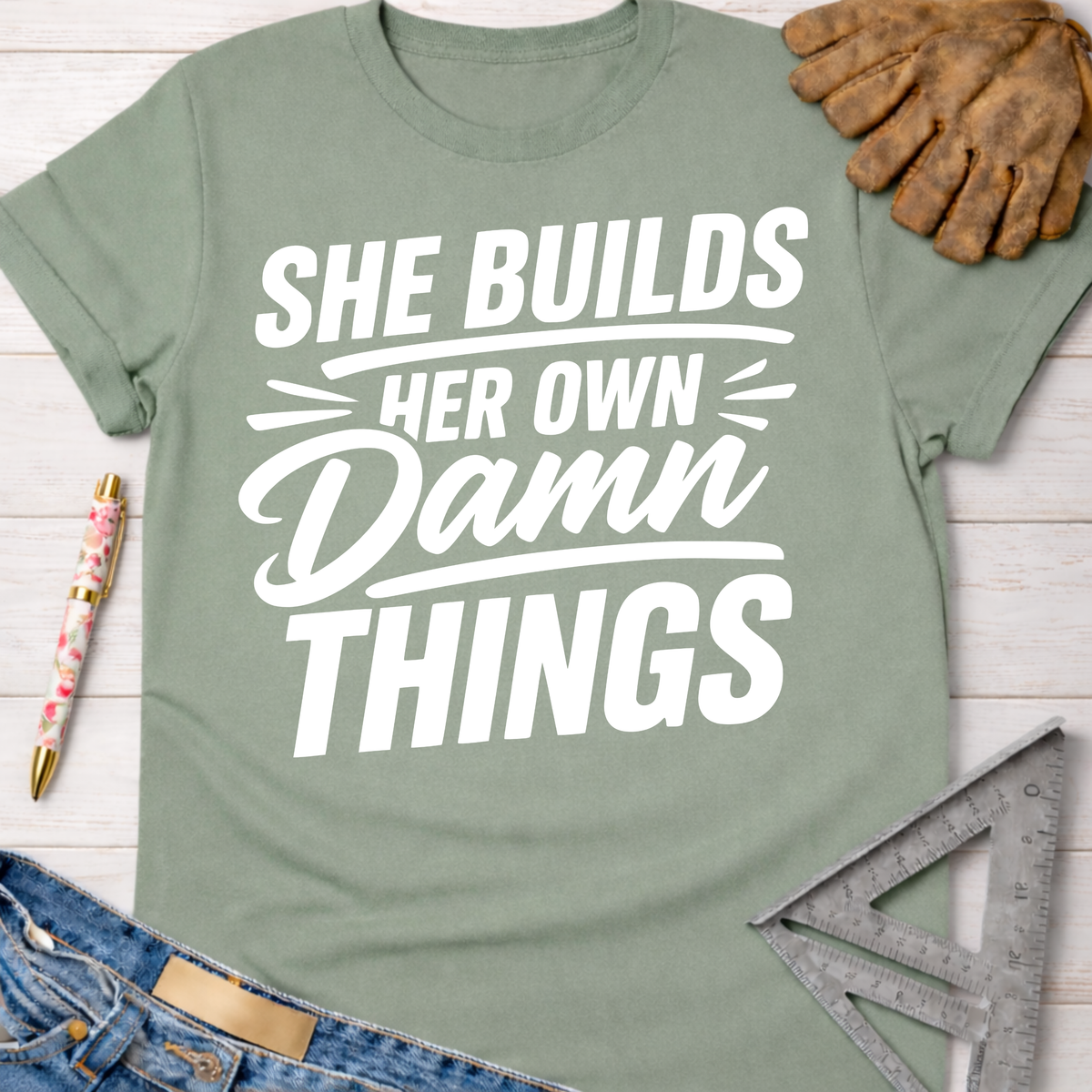 Sage green "She Builds Her Own Damn Things" graphic tee, women's funny woodworking shirt for makers and DIY builders.