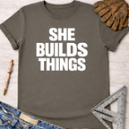 Women's funny woodworking graphic tee shirt for female woodworkers, makers, and DIY builders — Sawdust & Ponytails. Dark gray cotton t-shirt with "SHE BUILDS THINGS" in white text.