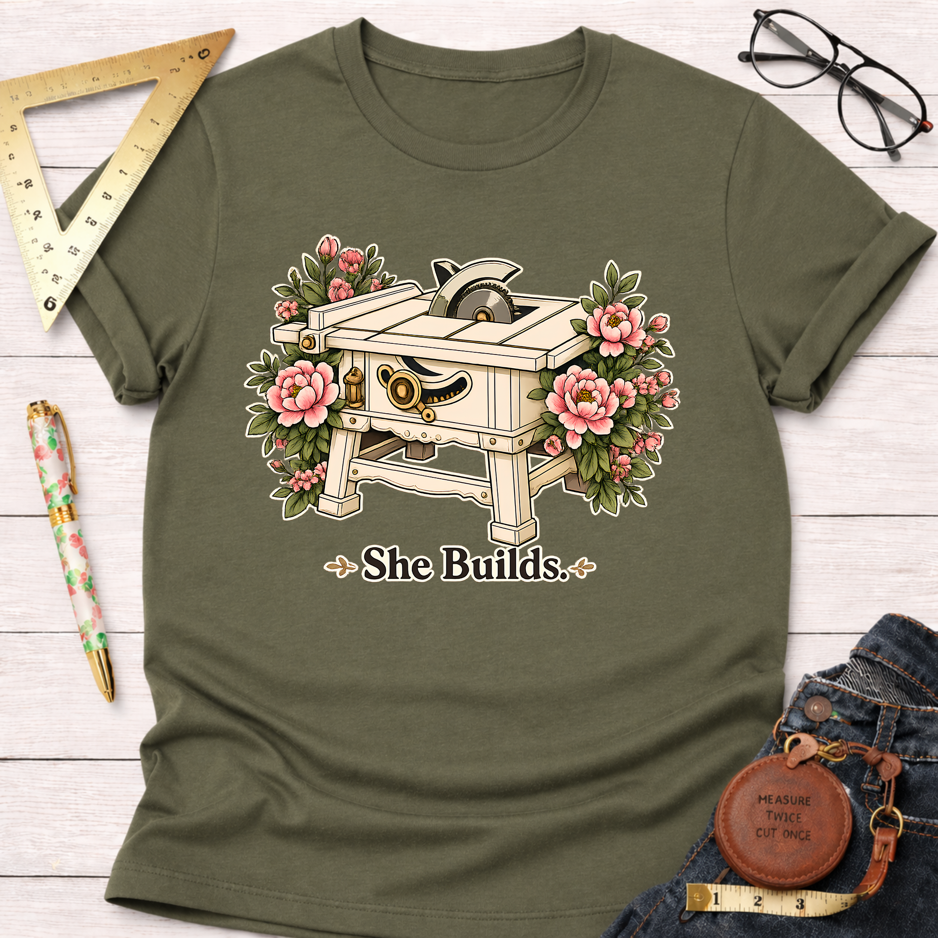 Olive green "She Builds" t-shirt with a table saw and pink floral design.