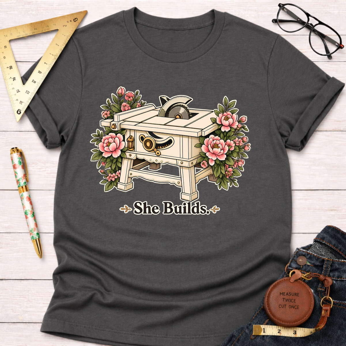 Charcoal gray "She Builds" t-shirt featuring a table saw surrounded by pink peonies.