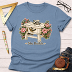 Light blue "She Builds" t-shirt with a table saw and pink floral design.