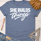 Blue cotton "She Builds Things" graphic tee, with work gloves, jeans, pen, and speed square. Women's funny woodworking graphic tee shirt for female woodworkers, makers, and DIY builders — Sawdust & Ponytails.