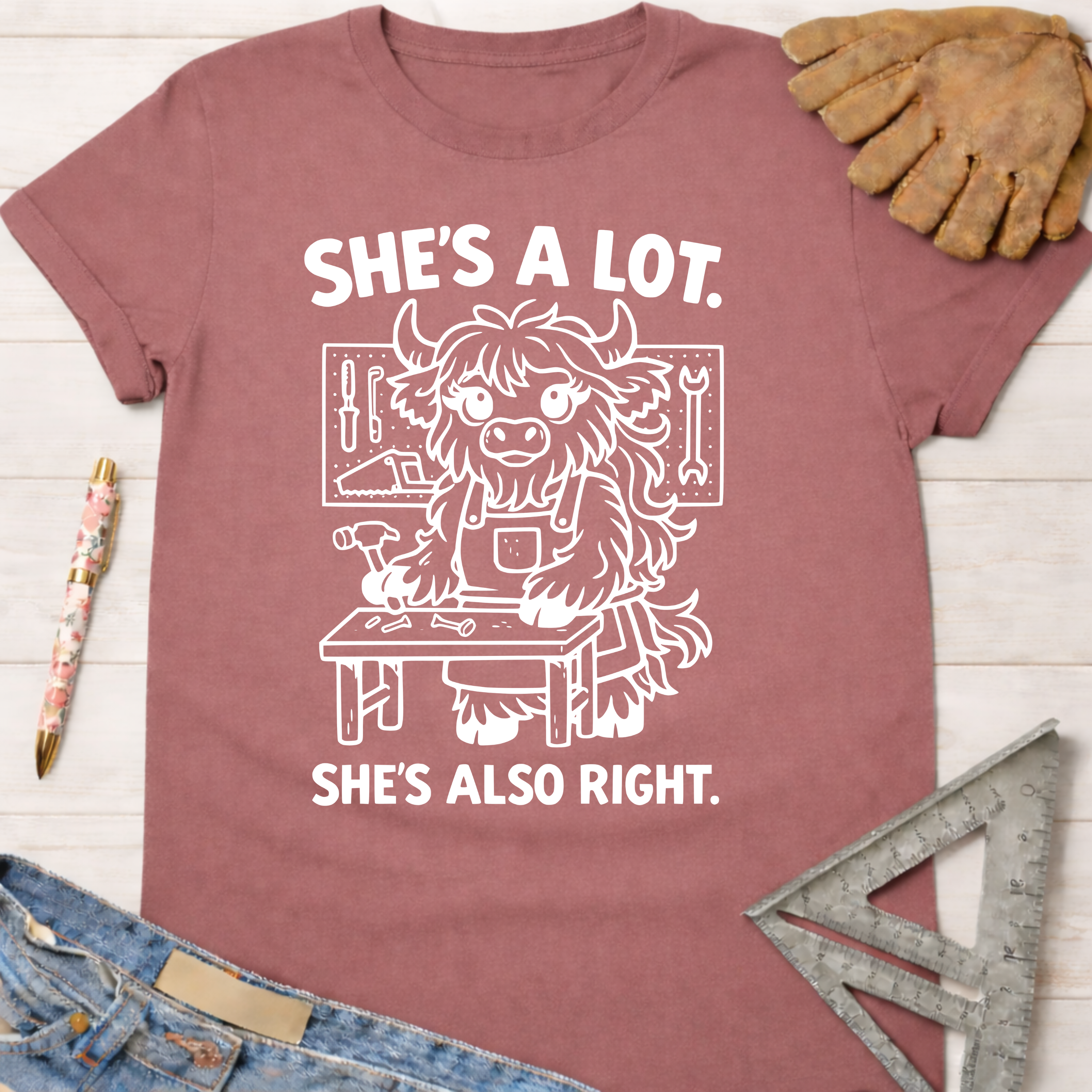 Women's funny woodworking graphic tee shirt for female woodworkers, makers, and DIY builders — Sawdust & Ponytails. Mauve cotton tee with "She's A Lot. She's Also Right." and a cartoon yak at a workbench.