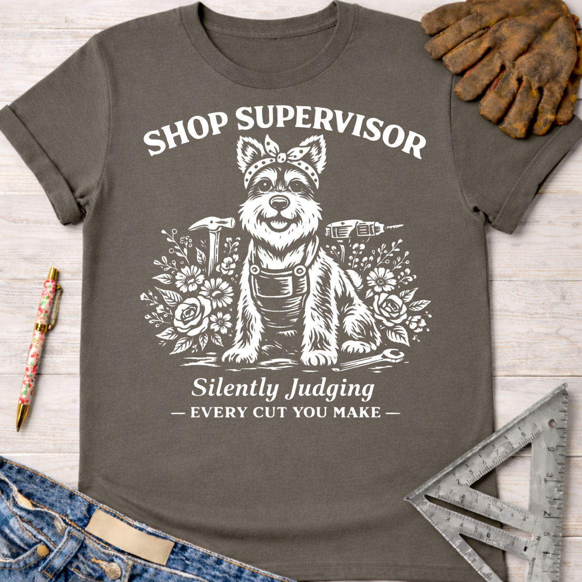 Women's funny woodworking graphic tee shirt for female woodworkers, makers, and DIY builders — Sawdust & Ponytails. Dark gray cotton tee with white graphic of a dog in a bandana and overalls, surrounded by tools and flowers, text "Shop Supervisor Silently Judging Every Cut You Make".