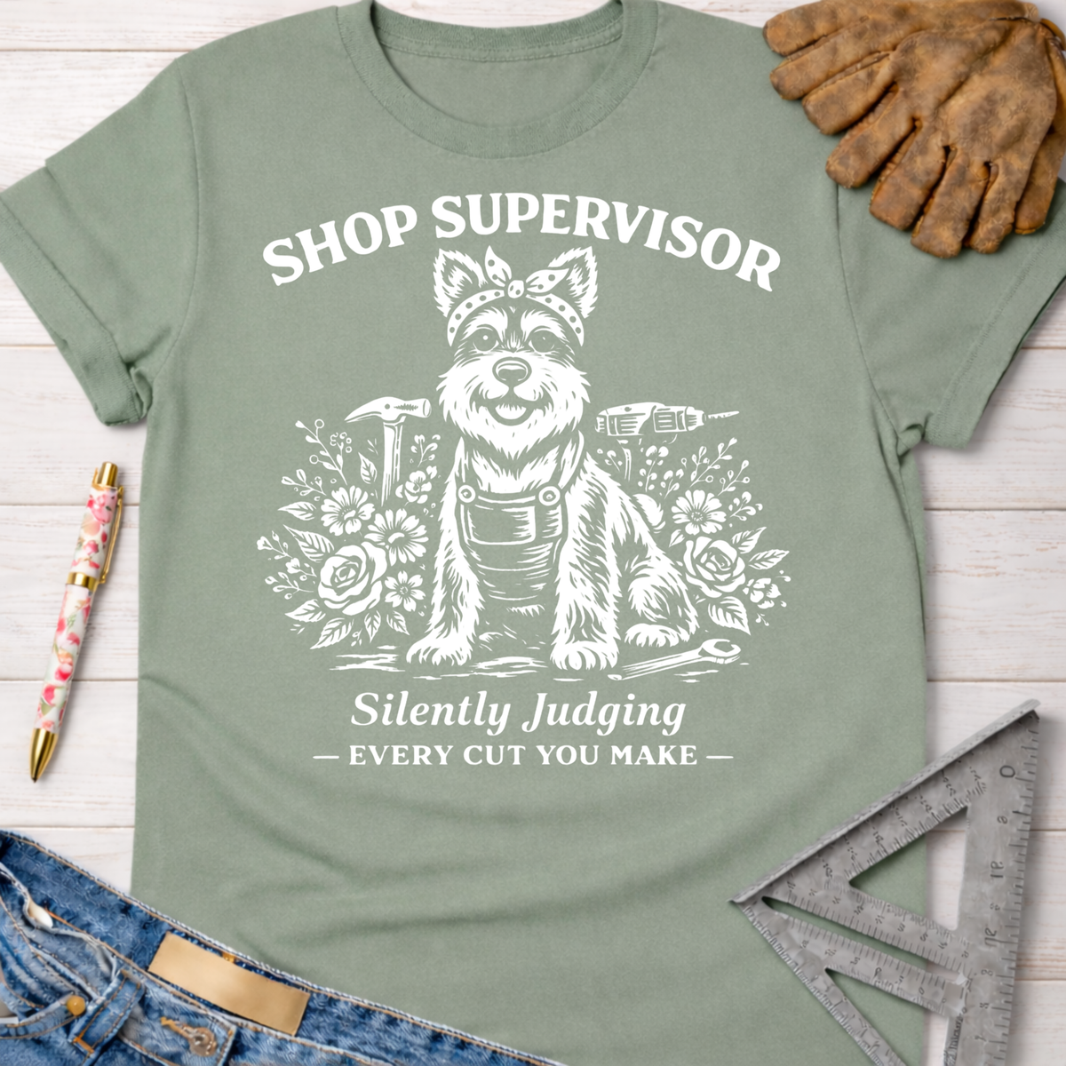 Women's funny woodworking graphic tee shirt for female woodworkers, makers, and DIY builders — Sawdust & Ponytails. Sage green cotton tee with white graphic of a dog in overalls, "Shop Supervisor Silently Judging" text.