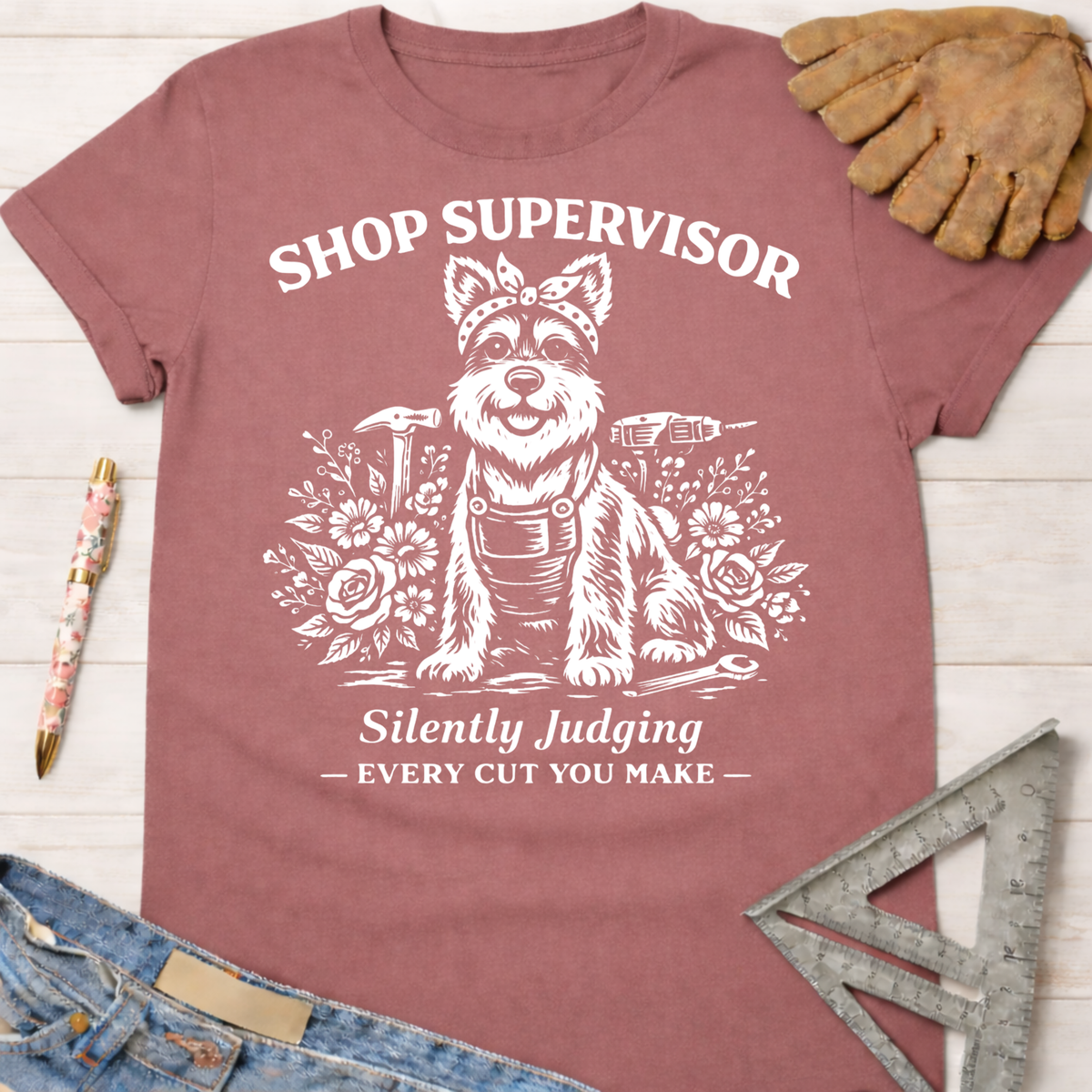 Women's funny woodworking graphic tee shirt for female woodworkers, makers, and DIY builders — Sawdust & Ponytails. Mauve cotton tee with "Shop Supervisor Silently Judging Every Cut You Make" text and a dog wearing a bandana and overalls surrounded by tools and flowers.