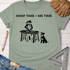 Women's funny woodworking graphic tee shirt for female woodworkers, makers, and DIY builders — Sawdust & Ponytails. Sage green cotton tee with "SHOP TIME = ME TIME" text and a graphic of a woman sawing wood with a dog.