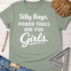Women's funny woodworking graphic tee shirt for female woodworkers, makers, and DIY builders — Sawdust & Ponytails. Sage green cotton tee with "Silly Boys. Power Tools Are For Girls." in white text.