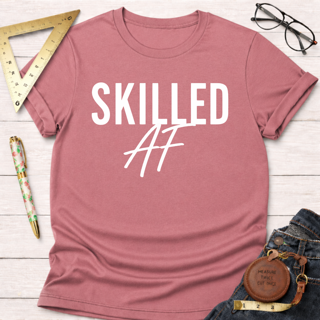 Skilled AF T-shirt in dusty rose pink cotton with white text, styled with jeans and workshop tools.