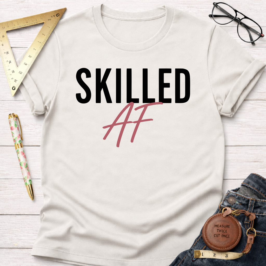 White cotton t-shirt with "Skilled AF" in black and pink text, styled with jeans, ruler, and glasses.