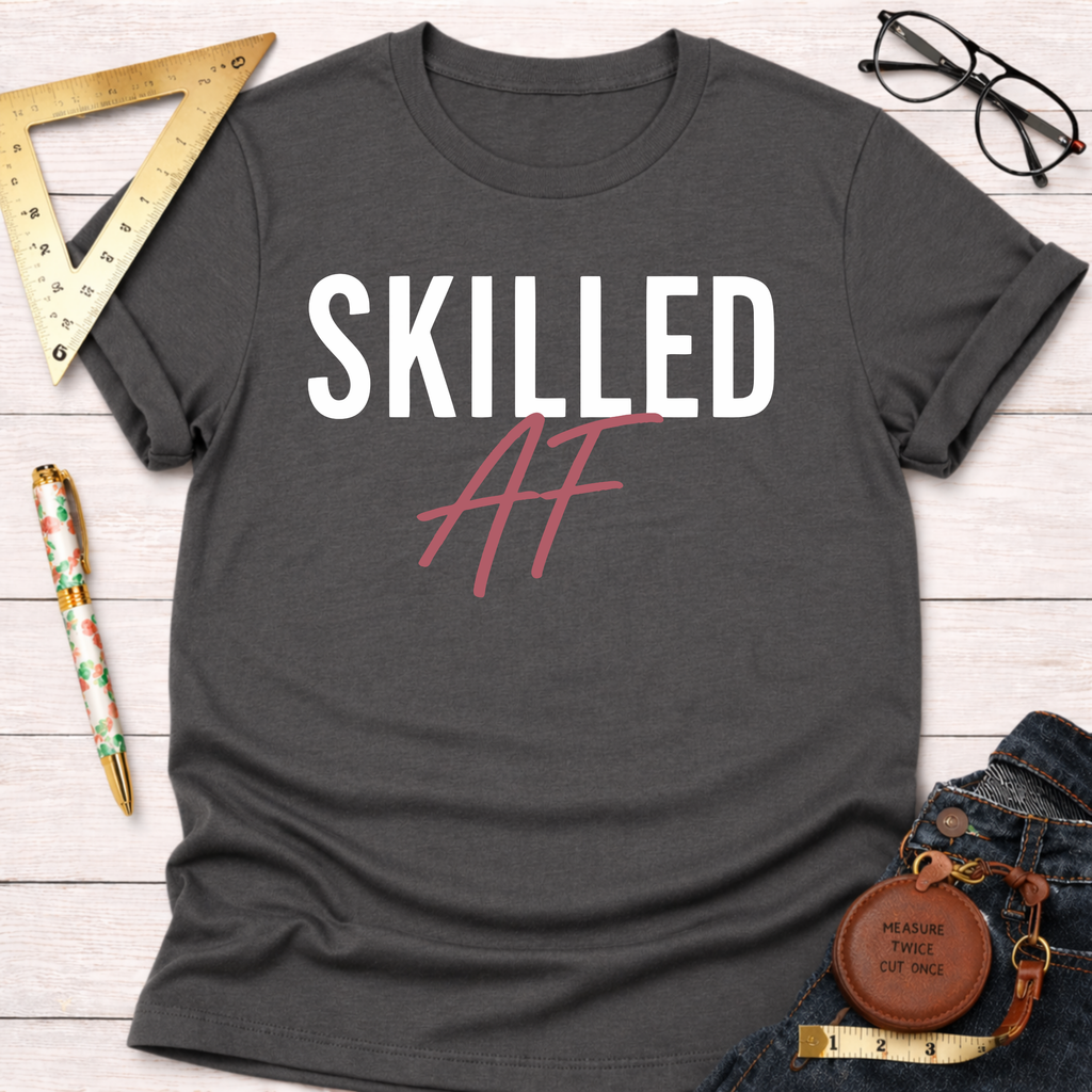 Charcoal gray cotton t-shirt with "SKILLED AF" in white and pink, styled with jeans and tools.