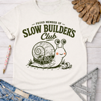 Women's funny woodworking graphic tee shirt for female woodworkers, makers, and DIY builders — Sawdust & Ponytails. Cream t-shirt with a "Slow Builder's Club" snail graphic.