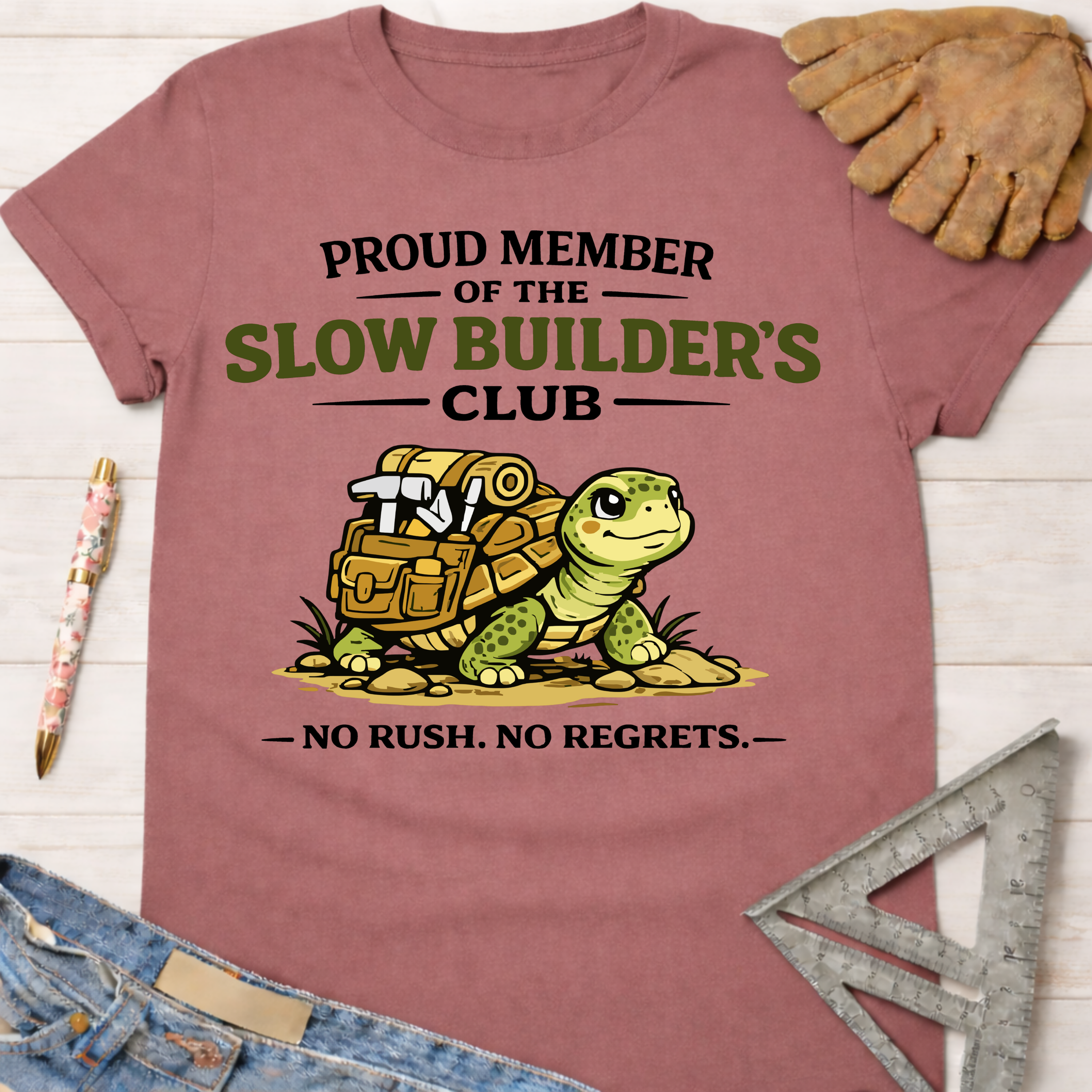 Women's funny woodworking graphic tee shirt for female woodworkers, makers, and DIY builders — Sawdust & Ponytails. Mauve cotton tee with "Proud Member of the Slow Builder's Club" text and a turtle carrying tools.