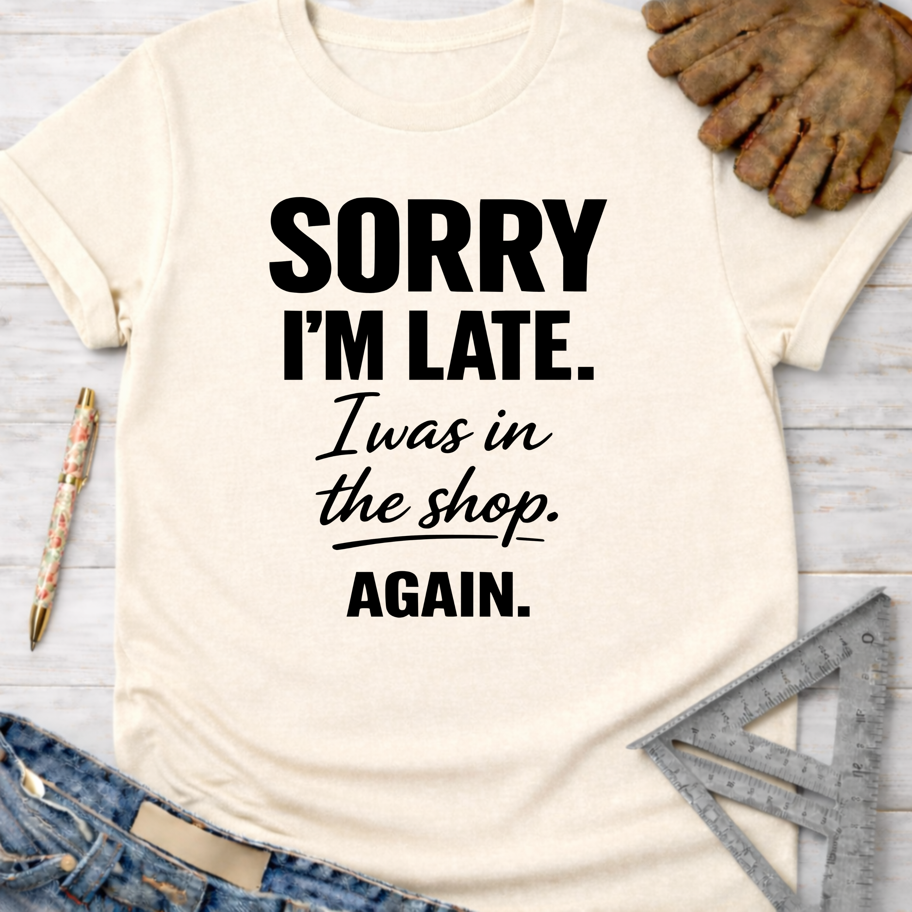 Women's funny woodworking graphic tee shirt for female woodworkers, makers, and DIY builders — Sawdust & Ponytails. Cream t-shirt with "Sorry I'm Late. I was in the shop. AGAIN." in black text.