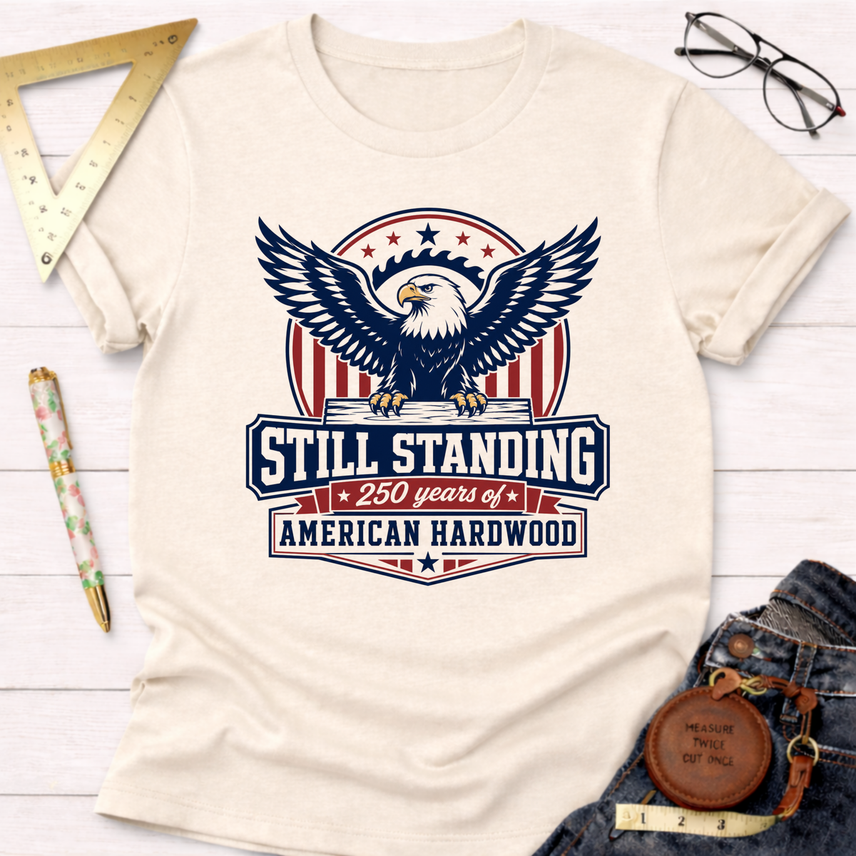 Cream t-shirt with a "Still Standing American Hardwood" eagle graphic in red, white, and blue.