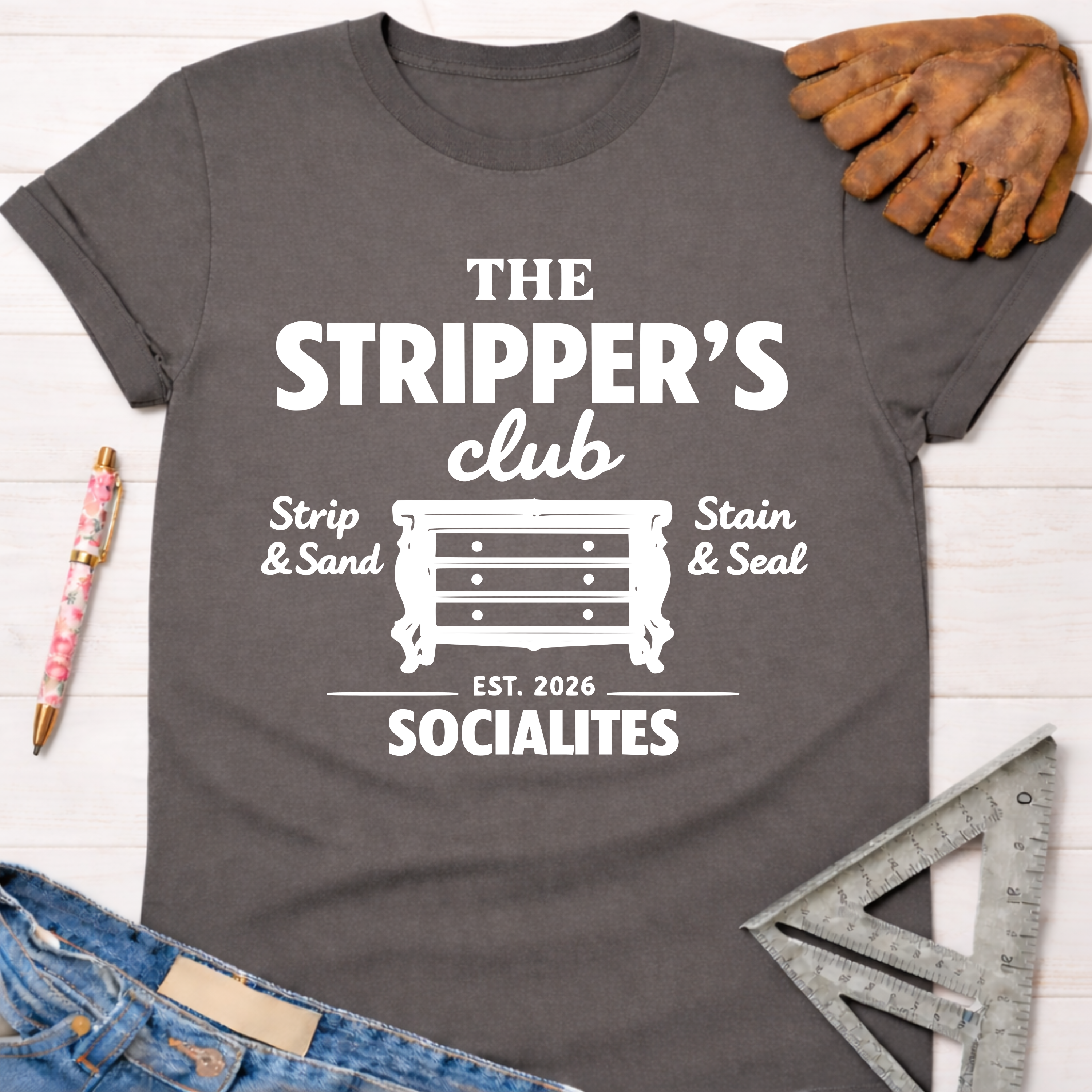 Women's funny woodworking graphic tee shirt for female woodworkers, makers, and DIY builders — Sawdust & Ponytails. Dark gray cotton tee with "The Stripper's Club Socialites" graphic, a dresser icon, and "Strip & Sand, Stain & Seal.